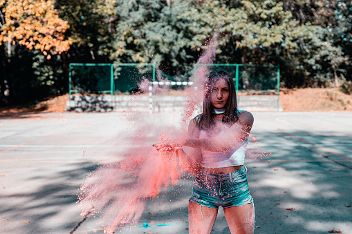 Young casually dressed woman having fun with colored powder in the urban sports court in the city on a sunny summer day outdoors