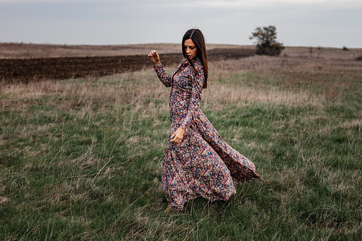 Beautiful young woman wearing a fashionable floral pattern long dress with long sleeves on a lovely autumn day in nature