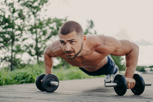 młody zmotywowany sportowiec stoi w desce, trenuje mięśnie sztangą, koncentruje się na dystansie z determinacją, ma nagi tułów, ma silne muskularne ciało. sportowiec kulturysta na zewnątrz - muscular build body building shirtless one person zdjęcia i obrazy z banku zdjęć