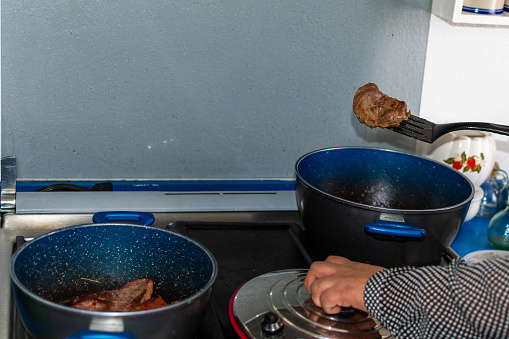 hands of woman making some meat on a blue cooking pot