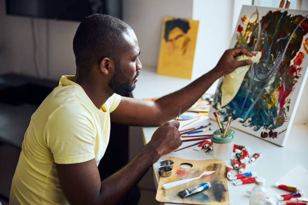мужчина вытирает краску с картинки - easel adult art creativity стоковые фото и изображения