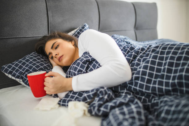 istock Sleeping young sick girl lying on a bed with cold and high fever and drinking tea 1292130963