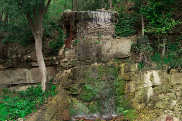 istock Waterfall in the forest, water flows down the stones 1292134501