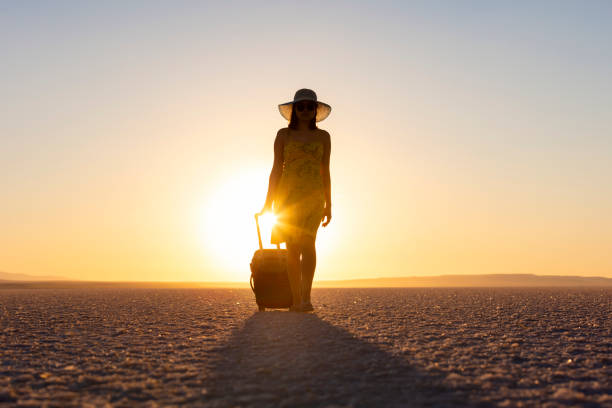Young woman with suitcase walking on sunset
