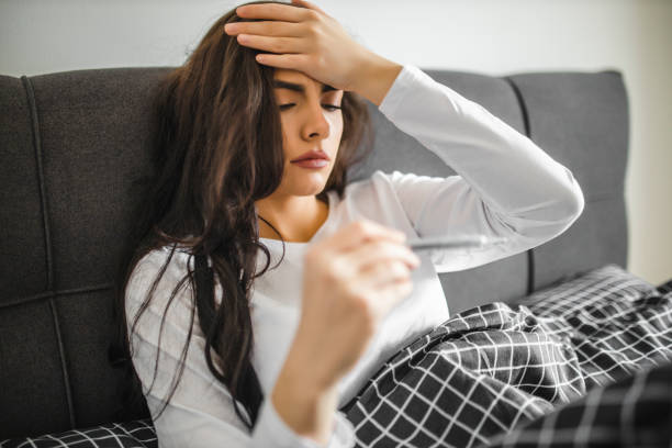istock Woman being sick, having flu, lying on bed and looking at temperature on thermometer 1292135451