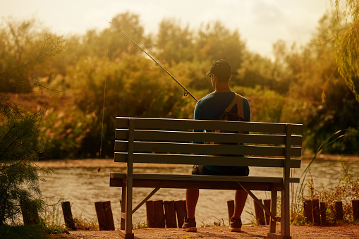 Rear view of man feeling patient at the lake whilst fishing, feeling relaxed doing his hobby, sitting on bench