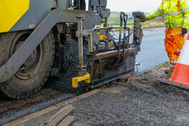 Asphalt mix being put down from an asphalt paver machine Road repairs taking place. Hot, black asphalt concrete mix being put down as a new road surface. It is being spread from an asphalt paver finisher, which compacts the mix and puts it down to a set level. A construction worker wearing high visibility workwear is using a control panel to distribute the material evenly. put down stock pictures, royalty-free photos & images