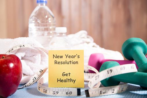 New Years resolution to get healthy in the coming year.  Group of objects include:  note pad, big red apple, tape measure, dumbbells, bottled water, running shoes and towel.     
 Base is a blue exercise mat.  Concept of an individual preparing items for an exercise.