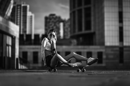 sports young woman at sunny park sitting on skateboard, meditating with closed eyes, monochrome