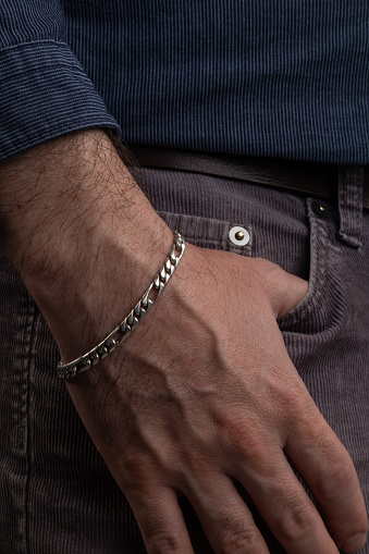 hand of a person with bulging veins inside pants pocket, wearing silver jewelry, wearing bracelet, studio