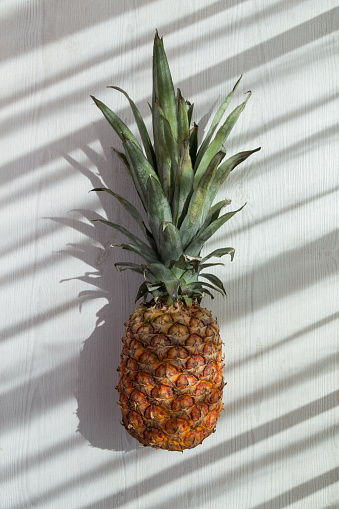 a delicious fresh pineapple with leaf on a white background, sun and shadow, studio shot of fruit, healthy life