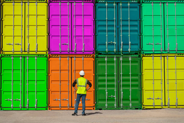 istock Engineer man with yellow crash helmet and worker west checking cargo freights in front of colorful cargo container stacks in shipping port 1292158441
