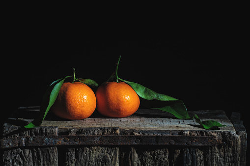 Two orange tangerines with leaves on an old wooden box. Low-key photography.