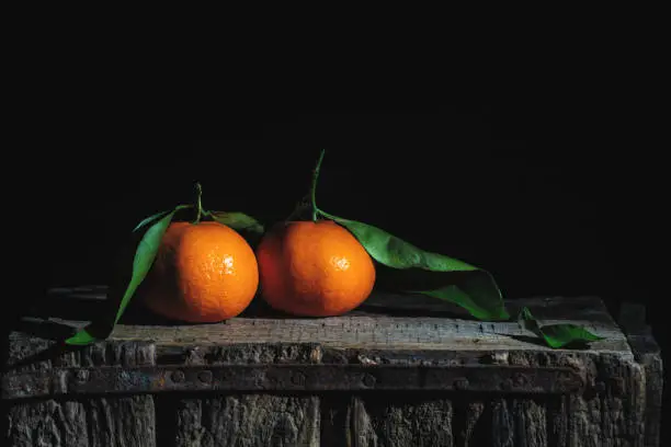 Photo of Two orange tangerines with leaves on an old wooden box. Low-key photography.