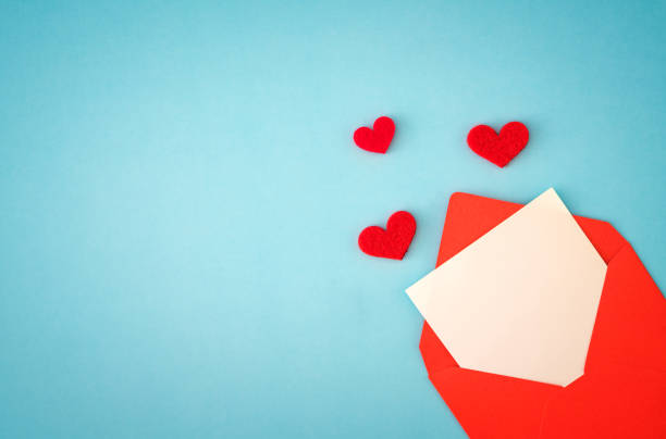 istock Red paper envelope with blank white note mockup inside and Valentines hearts on blue background 1292165195