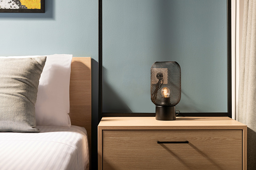 Primer plano de la moderna lámpara de bombilla de metal negro en la mesa de noche del dormitorio de madera en el interior de la habitación gris de estilo contemporáneo con cama de madera de pino y ropa de cama de algodón blanco photo