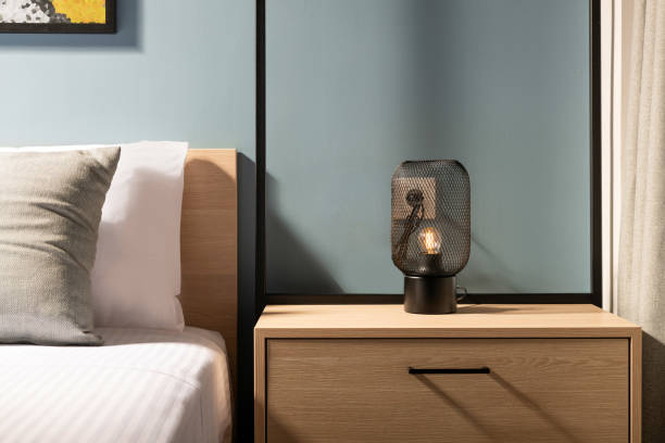 primer plano de la moderna lámpara de bombilla de metal negro en la mesa de noche del dormitorio de madera en el interior de la habitación gris de estilo contemporáneo con cama de madera de pino y ropa de cama de algodón blanco - hotel room bedroom hotel contemporary fotografías e imágenes de stock