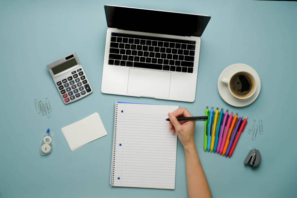istock Student is writing essay on the notebook with the computer laptop and pen on blue background. 1292175241