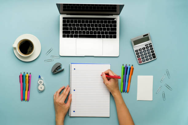 istock Student is writing essay on the notebook with the computer laptop and pen on blue background. 1292175263