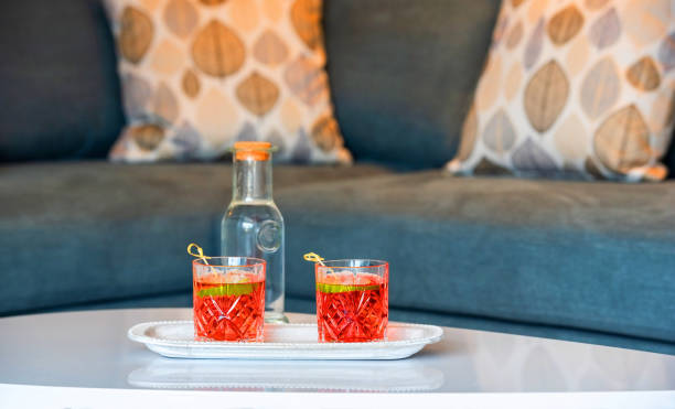 istock Closeup of two campari glasses on white table top surface in lounge interior blur background with grey sofa and autumn pillows 1292176948