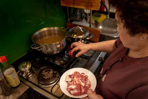 Overhead view of Asian senior Chinese grand mother placing marinated pork into pot during the preparation of Chinese New Year reunion dinner