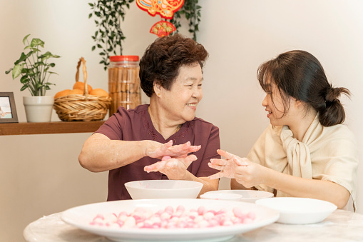 Asian senior adult grandmother teaching grand daughter how to make TangYuan dumpling during Chinese New Year reunion dinner preparation