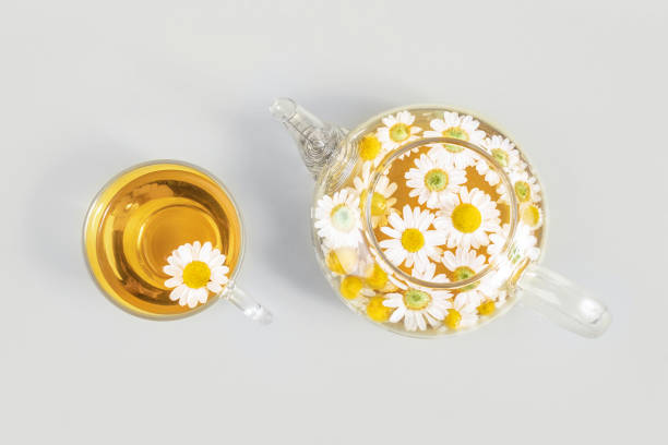 tazza di tè e teiera trasparente con fiori di camomilla su sfondo giallo. il tè alla camomilla avvantaggia il tuo concetto di salute. vista dall'alto. colori alla moda 2021 - pantone 2021 foto e immagini stock