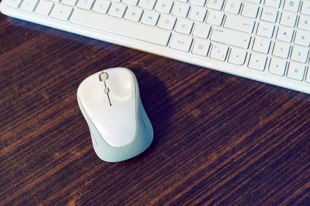 A white computer mouse and keyborad on a wooden desk A white computer mouse and keyborad on a wooden desk of an office. keyborad stock pictures, royalty-free photos & images