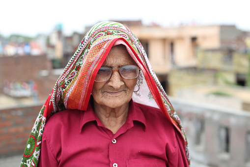 Old woman of Indian ethnicity standing of rooftop at home outdoors and she smiling to the camera.