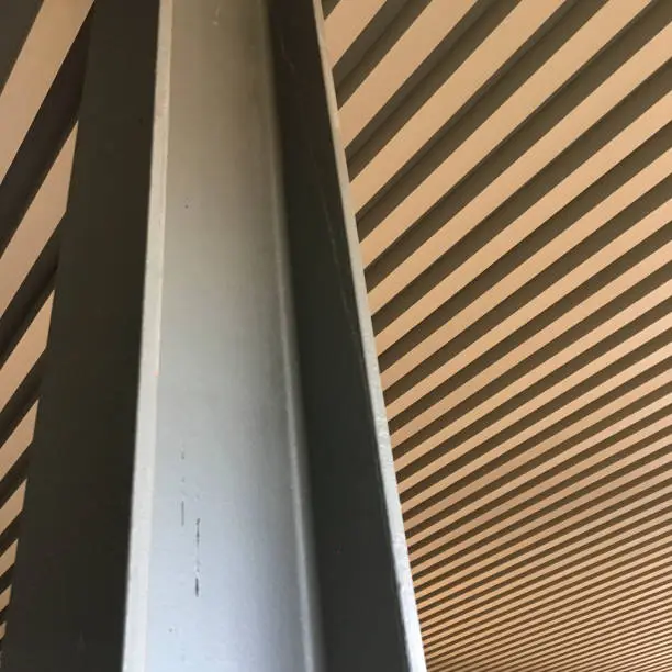 The ceiling of a straight pattern can be seen behind the h-beam pillars of a modern building.