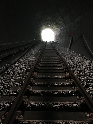 Inside a dark tunnel with railroad tracks, we can head out to bright light.
