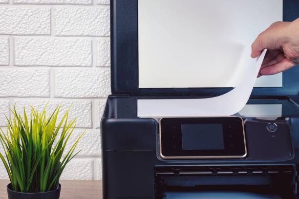 istock A young man's hand lays a stack of white paper on the scanning surface of a black printer. Green plant in a pot on a wooden table. 1292201941