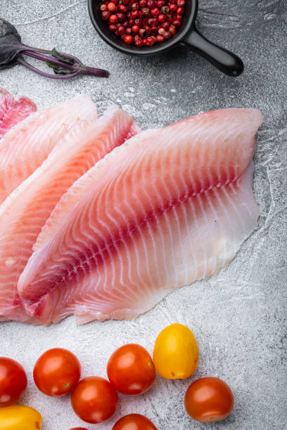 istock Raw white fish tilapia with basmati rice and cherry tomatoes ingredients, on gray background, top view 1292205355
