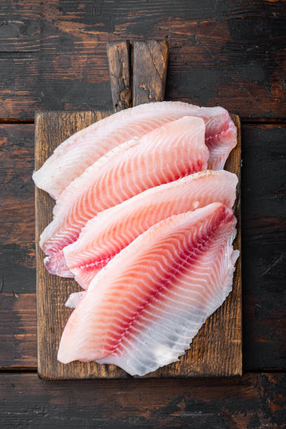 istock Tilapia fish skinless meat, on dark wooden background, top view 1292205366