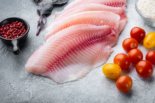 istock Raw white fish tilapia with basmati rice and cherry tomatoes ingredients, on gray background 1292206801