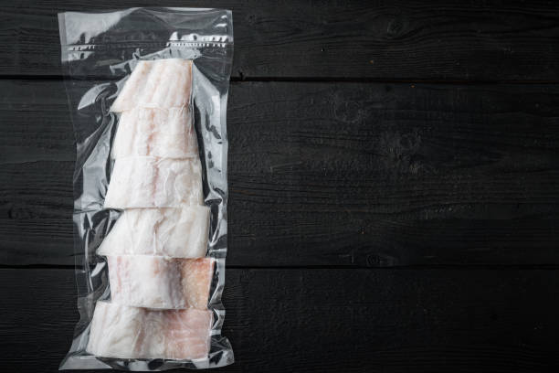 istock Raw haddock fish skinless, plastic vacuum packaged, on black wooden background, top view with copy space for text 1292206989