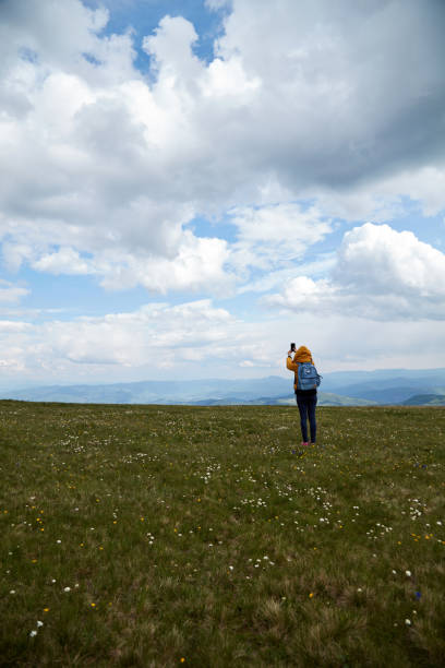 istock One woman using cellphone on a big meadow and landscape mountain top view. 1292215710