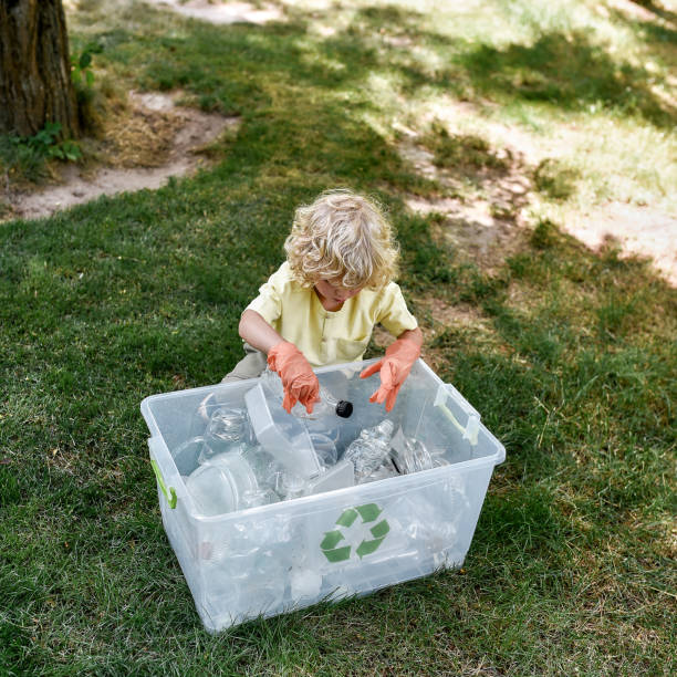 istock Cute little caucasian boy wearing rubber gloves throwing plastic waste into recycle bin while cleaning in the forest or park 1292219586
