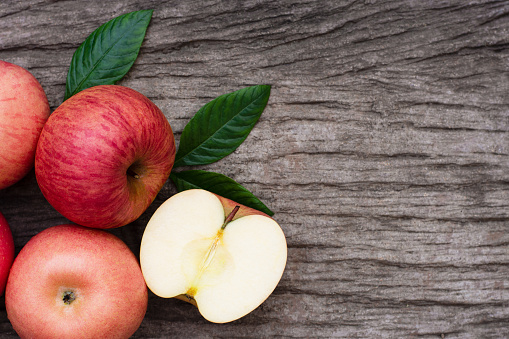 Pink fuji apple with cut in half slice and green leaf on wood table background. Top view. Copy space for text.