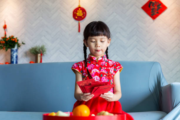 dolce ragazza cinese con il qipao tradizionale celebra il capodanno cinese a casa - cheongsam chinese culture indoors looking at camera foto e immagini stock