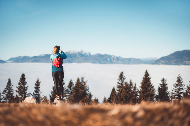 Caucasian woman mountaineer taking photos. Sun in the mountains and fog in the valley. Beautiful autumn winter day in the mountains.