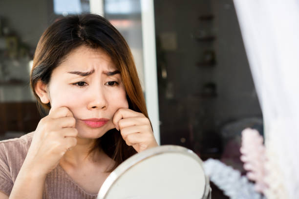 istock worried Asian woman hand pulling her fat skin on cheeks ,checking her face on mirror 1292228356