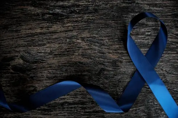 Photo of Top view of dark blue ribbon on wooden background with copy space. Colon, stomach, colorectal cancer, arthritis, ards acute respiratory distress syndrome awareness and child abuse prevention concept.