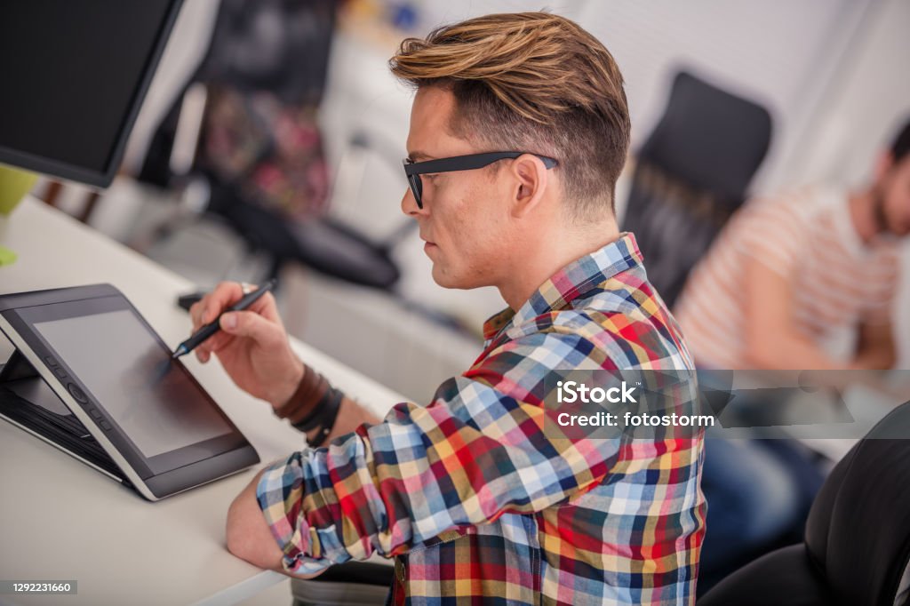 Using a tablet device to expedite on pressing tasks at the workplace Tilt, side view of hardworking graphic designer using his tablet to create a new visual piece for his company. Animator Stock Photo