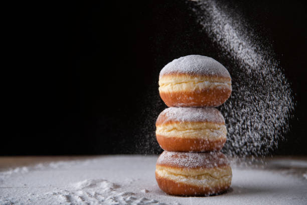 European donut sprinkled with powdered sugar on black background. Three donuts filled with marmelade sprinkled with powdered sugar. Traditional Mardi Gras or Fat Tuesday doughnut. deep fried photos stock pictures, royalty-free photos & images