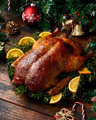 Roasted Christmas duck with decoration, gifts, green tree branch on wooden rustic table.