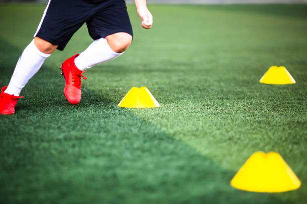 istock Selective focus to cone marker with blurry boy soccer player is jogging on green artificial turf. 1292245650