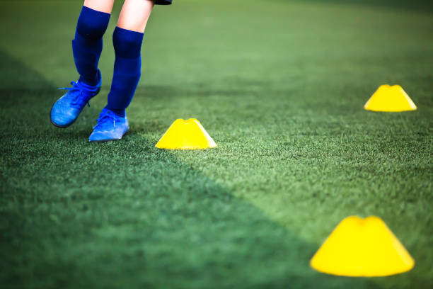 istock Selective focus to cone marker with blurry boy soccer player is jogging on green artificial turf. 1292245652