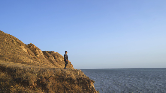 The man standing on the mountain cliff on the seascape background