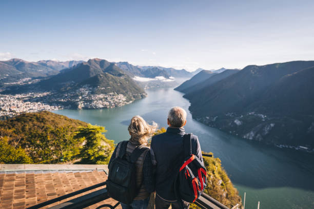 Mature couple hike above lake Lugano in the morning They relax at viewpoint and look off to distant scene couple adventure activity adult stock pictures, royalty-free photos & images